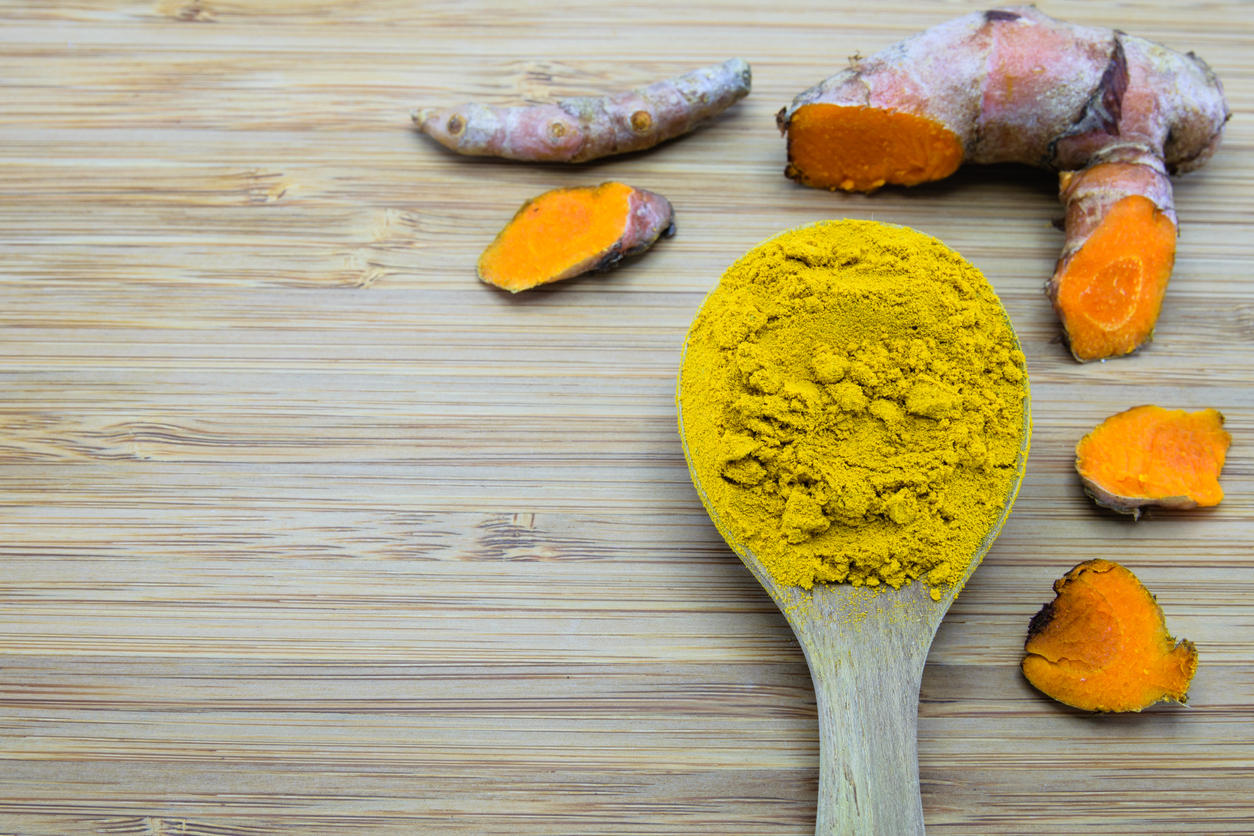 turmeric powder in wood spoon and turmeric root on wood background